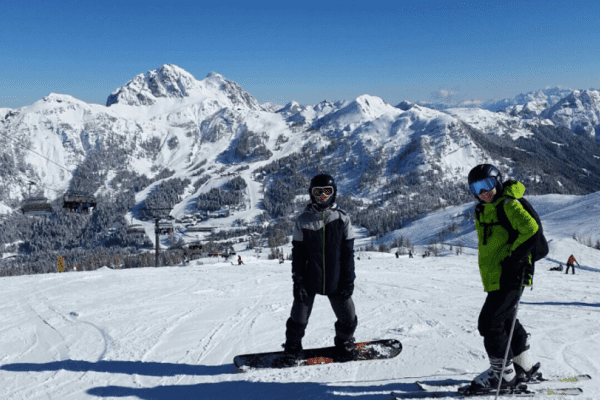 Zwei Jungs mit Ski und Snowboard auf Piste