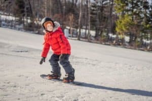 Junge in roter Jacke auf einem Snowboard