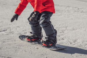 Junge in roter Jacke auf Snowboard in Snowboardcamps