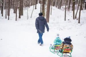Vater zieht zwei Kinder auf dem Schlitten im Skiurlaub Schwarzwald