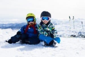 Zwei kleine Jungs sitzen fröhlich im Schnee und freuen sich