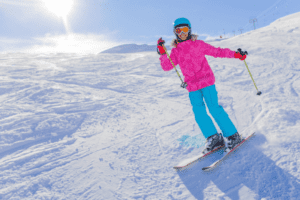 Mädchen in pinker Jacke winkt beim Skifahren