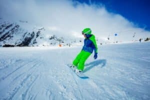 Junge in grüner Jacke auf dem Snowboard