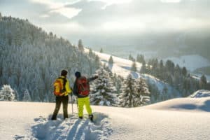 Zwei Männer machen Pause im Schnee und zeiegen ins Tal