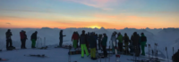 Viele Skifahrer bei Sonnenuntergang auf dem Berg